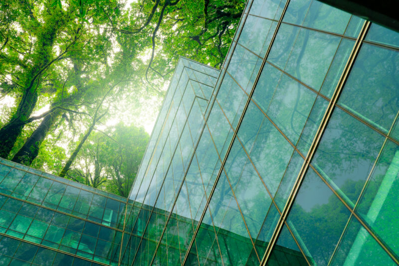 Edificio corporativo moderno con fachada de vidrio rodeado de árboles, que refleja la integración entre operación inmobiliaria y sostenibilidad ambiental.
